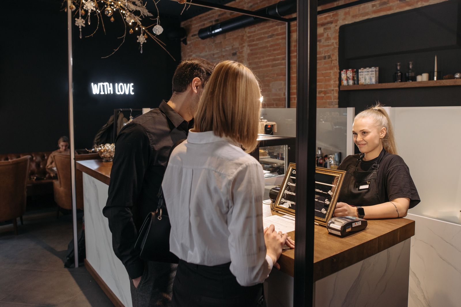 Cafe staff member serving two customers at the counter beside a payment terminal