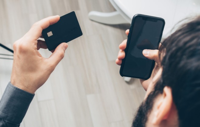 A customer holding a card and a phone to pay over the phone